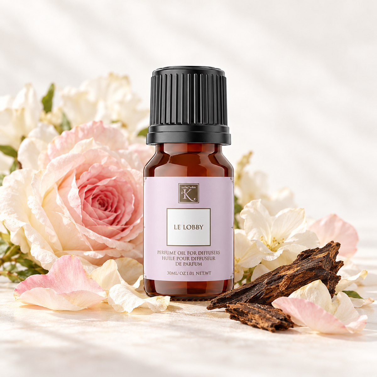 Huile parfumée Le Lobby 30 ml, mise en scène avec des fleurs délicates et du bois pour évoquer ses notes florales et d’oud.